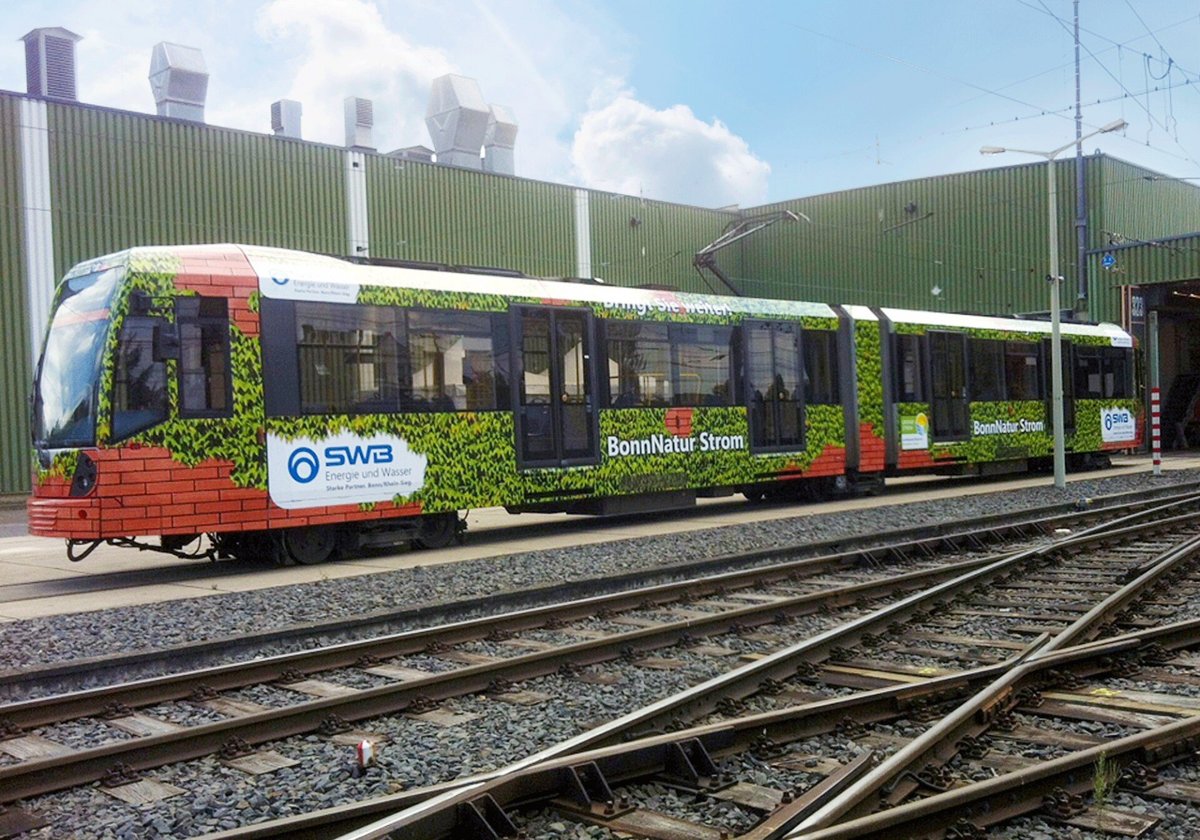 Straßenbahn mit Werbebeschriftung für „BonnNatur Strom“ und SWB Energie und Wasser, gestaltet mit einer grünen Pflanzenoptik und Backstein-Elementen, die Nachhaltigkeit und Naturverbundenheit symbolisieren.